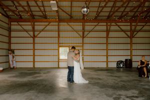 Bride and groom share first dance in a rustic barn venue with disco ball lighting.