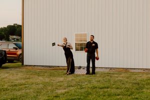 Two wedding guests stand outside a white barn building during a summer outdoor wedding reception.