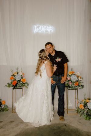Bride and groom pose together in front of a neon sign reading their last name at wedding reception.