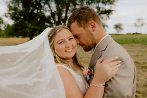 Groom tenderly nuzzles bride as her veil flows in the breeze during a romantic outdoor wedding portrait.