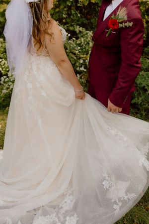 Close-up of bride in lace wedding gown train holding hands with groom in burgundy suit.