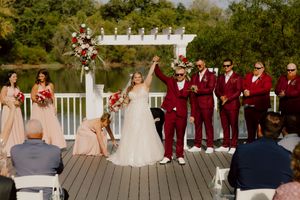 Newlyweds celebrate with raised hands as wedding party cheers on a lakeside deck after the ceremony.