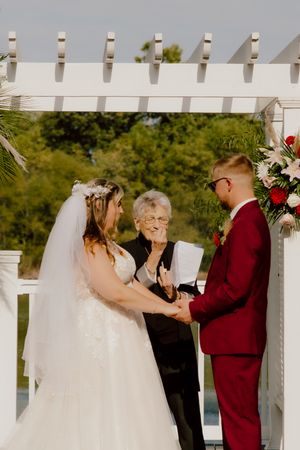 Bride and groom exchange vows under a white pergola with floral arrangements at a waterfront ceremony.