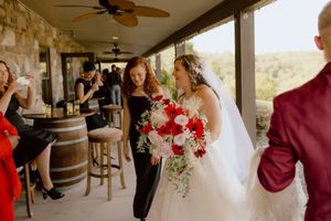 Bride carrying red and white bouquet walks with bridesmaid on venue patio.