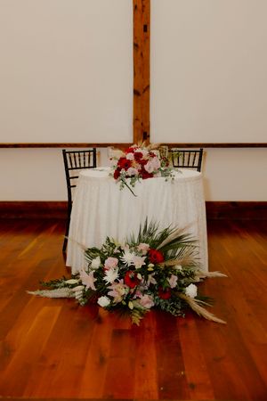 Elegant sweetheart table with white linen and lush red and pink floral arrangements.