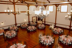 Elegant wedding reception hall with round tables draped in pink linens, dark wood floors, and chandelier lighting.
