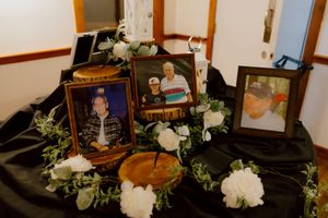 Memorial table with framed photos, white floral arrangements, and keepsakes displayed on black fabric.