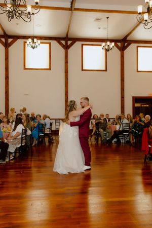 Bride and groom share their first dance on a wooden floor in an elegant barn wedding venue.