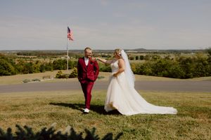 Bride and groom share a joyful first look moment on a sunlit hilltop with American flag in background.