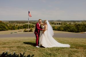 Bride and groom share a romantic moment on a hilltop with an American flag and scenic countryside backdrop.