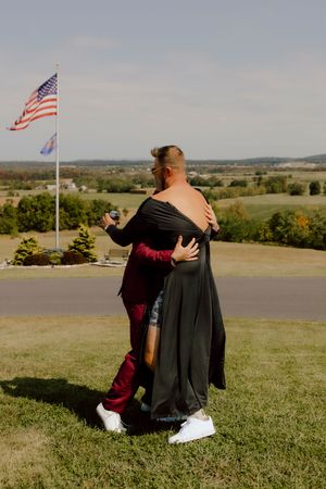 Couple sharing an embrace on a grassy hilltop with American flag and rolling countryside in background.
