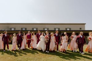 Wedding party walking together outside barn venue, bridesmaids in blush gowns and groomsmen in burgundy suits.