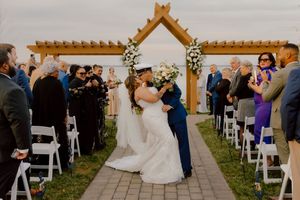 Military groom kisses bride at outdoor wedding ceremony under wooden pergola arch.