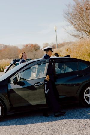 Military groom in dress uniform opens car door for bride on sunny wedding day.
