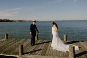 Bride and groom share first look moment on wooden dock overlooking calm blue water on wedding day.