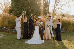Wedding party celebrates outdoors in golden sunset light with bride, groom, and attendants toasting.