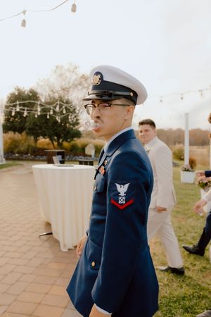 Navy serviceman in dress uniform with white cap and medals at an outdoor wedding reception.