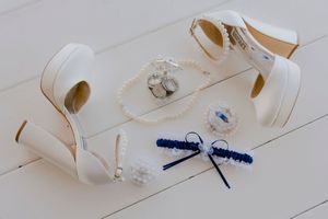 White bridal heels, pearl bracelet, blue garter, and wedding accessories flat lay.