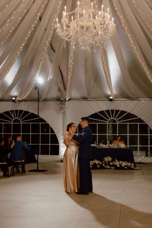 Couple shares first dance under crystal chandelier in draped wedding tent.