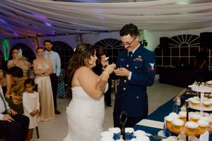 Military groom and bride cutting wedding cake at elegant tent reception.