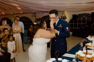 Bride feeds cake to uniformed military groom at wedding reception.