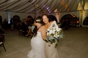 Bride embraces guest while holding white and green bridal bouquet.