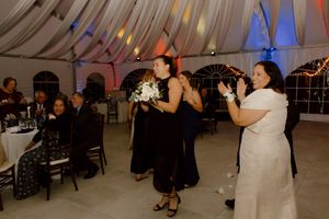 Bridesmaids in black dresses celebrate bouquet toss at wedding reception.