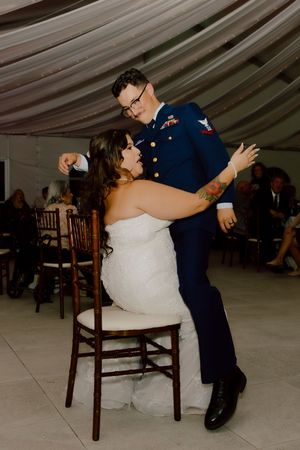Military groom dips bride in chair during fun wedding reception dance.