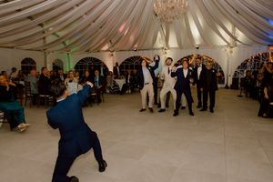 Groomsmen catching the garter toss on the dance floor at an elegant tented wedding reception.