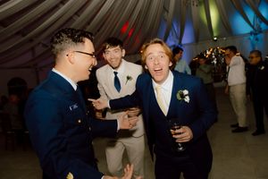 Three men in formal attire laughing and celebrating at a wedding reception party.