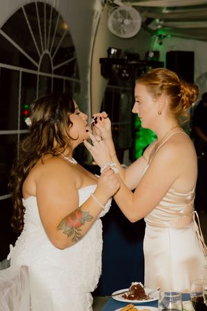 Two brides feeding each other wedding cake during their romantic same-sex wedding reception.