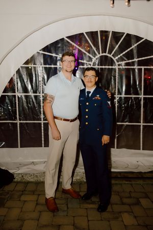 Two men posing together at a wedding reception, one wearing a military dress uniform.