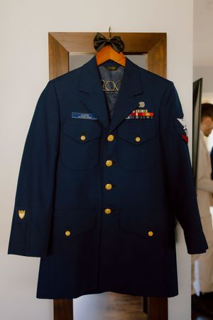 Navy blue Coast Guard dress uniform with gold buttons and service ribbons hanging on wooden door.