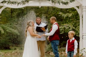 A bride and groom hold hands at an outdoor altar with a young ring bearer standing nearby.