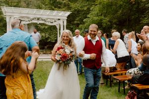 A joyful newlywed couple walks back up the aisle together after their outdoor wedding ceremony.
