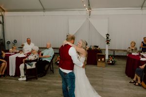 Bride and groom sharing first dance in white tent reception hall with guests seated nearby.