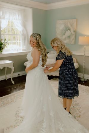 Mother helps bride in lace wedding gown with her dress in an elegantly decorated bridal suite.