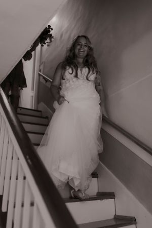 Black and white photo of a smiling bride in a strapless tulle gown descending a staircase.