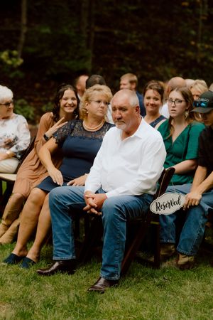Wedding guests seated on chairs at an outdoor ceremony, with a reserved sign on the front row.