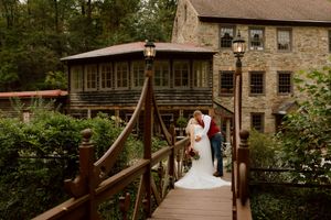 Bride and groom sharing a kiss on wooden bridge near rustic stone mill wedding venue.