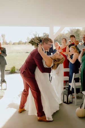 Groom dips bride during first dance at wedding reception with guests applauding.