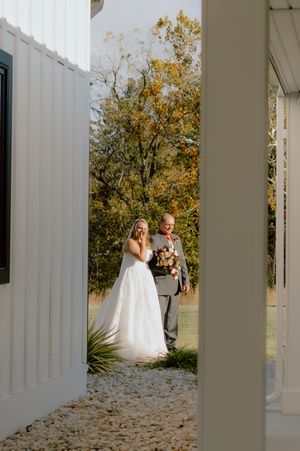 Bride in white gown walking with escort through garden path toward ceremony venue.
