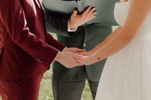 Couple holding hands during wedding ceremony with officiant in background.