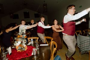 Wedding guests dancing in a lively conga line at festive reception dinner.