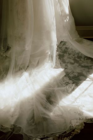 Ethereal white wedding dress with lace details illuminated by soft natural window light.