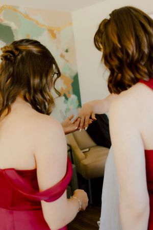 Two bridesmaids in red dresses admiring jewelry detail before the wedding ceremony.