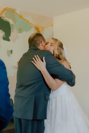 Bride in white wedding dress shares an emotional hug with her father on wedding day.