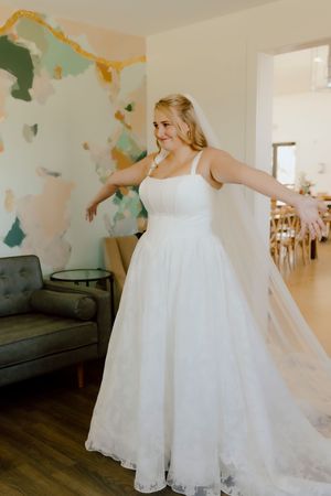 Smiling bride in white lace ball gown with veil poses in a decorated bridal suite.