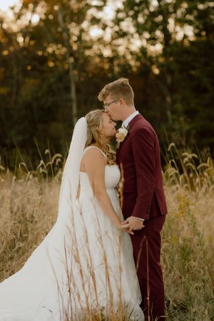 Bride and groom share a tender kiss in a golden autumn field at sunset.