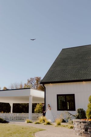 Bride and groom sharing a romantic moment outside a white barn wedding venue under blue sky.
